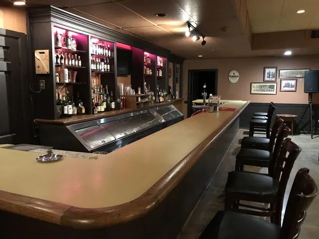 The long wooden bar with stools and lit bottle shelves at The Columbian