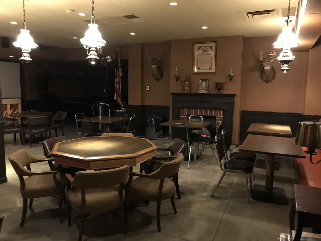 The seating end of the room with an octagonal card table, pendant lamps, dark chairs and a fireplace