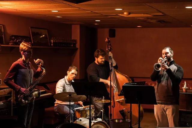 A jazz quartet with saxophone, drums, upright bass and trumpet playing in the corner of the room